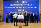 Two men in business attire stand beside a signed document as colleagues applaud behind them. A blue backdrop displays the names of both partner organizations.