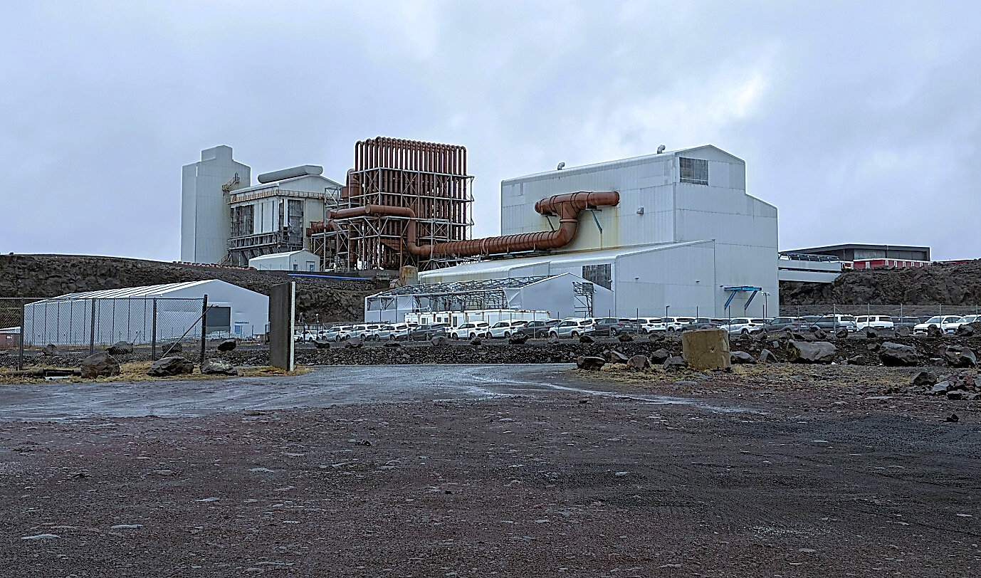Existing large scale industrial buildings and furnace hall at the Helguvík industrial site in southwest Iceland, illustrating the type of brownfield infrastructure that could potentially be refurbished for future low impact processing activities. The 8,376 m² industrial premises is a former furnace building which previously housed the silicon plant. The building has 5 floors with a lift shaft and 12.5–32.5 ton bridge cranes. The ground floor footprint is about 3,250 m², and each intermediate floor is about 1,430 m² of reinforced concrete slab. The building is on a concrete foundation, built of a steel frame and clad with corrugated sheet metal. The former furnace is a 33 MW electric arc furnace with various possibilities; its internal volume can be reduced, and it can be used for any operation requiring a process temperature of around 1,500 degrees or higher. The furnace building has very strong incoming power (33 kV stepped down to 400 V), glass fiber network, compressed air, four freshwater boreholes, and substantial infrastructure that can be used for almost any industrial production. Photo from Greenland Mines Ltd site visit at Helguvik. Existing large scale industrial buildings and furnace hall at the Helguvík industrial site in southwest Iceland, illustrating the type of brownfield infrastructure that could potentially be refurbished for future low impact processing activities. The 8,376 m² industrial premises is a former furnace building which previously housed the silicon plant. The building has 5 floors with a lift shaft and 12.5–32.5 ton bridge cranes. The ground floor footprint is about 3,250 m², and each intermediate floor is about 1,430 m² of reinforced concrete slab. The building is on a concrete foundation, built of a steel frame and clad with corrugated sheet metal. The former furnace is a 33 MW electric arc furnace with various possibilities; its internal volume can be reduced, and it can be used for any operation requiring a process temperature of around 1,500 degrees or higher. The furnace building has very strong incoming power (33 kV stepped down to 400 V), glass fiber network, compressed air, four freshwater boreholes, and substantial infrastructure that can be used for almost any industrial production. Photo from Greenland Mines Ltd site visit at Helguvik.