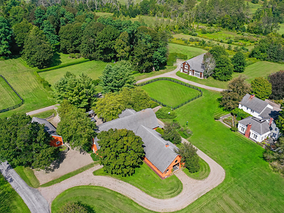 In addition to manicured grounds that include multiple paddocks, a private pond, gently rolling hills and sweeping views of the Catskill Mountains, the property includes a main residence (at right), 10-stall barn with upper-level apartments (center), carriage house (upper right) guesthouse (not pictured) and additional out-buildings for added storage.  HudsonValleyLuxuryAuction.com.