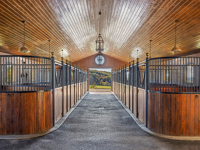 The center-aisle barn, designed by French firm Atelier Choiseul, features ten large stalls and is sited to capture a near-constant breeze, mitigating the need for excess sprays/repellants. There are also two tack rooms, a wash stall, feed room, hay loft, one half-bath and a handsome lounge with built-in wet bar. The barn’s upper level offers 2 staff apartments, while a large garage/workshop is located adjacent to the stalls. HudsonValleyLuxuryAuction.com.