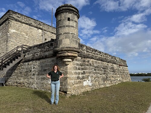 An individual standing with her hands on hips in front of a stone fort with water in the background. An individual standing with her hands on hips in front of a stone fort with water in the background.