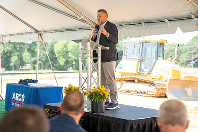 A representative addresses attendees at the OPW groundbreaking ceremony in Smithfield, North Carolina, with earthmoving equipment staged in the background ahead of construction on the new manufacturing facility.