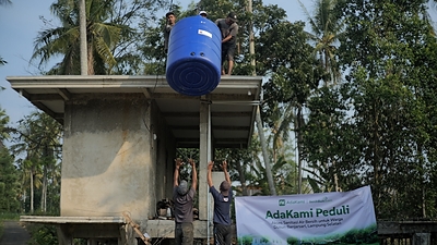 Workers install a large blue water tank on a structure as part of the AdaKami Peduli initiative to provide clean water access in Dusun Banjarsari, South Lampung