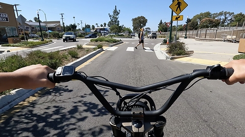 A first-person view from behind the handlebars of a teen entering an intersection on an ebike