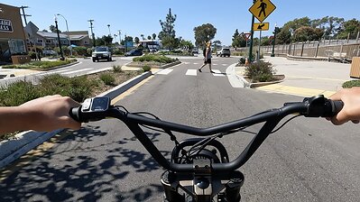A first-person view from behind the handlebars of a teen entering an intersection on an ebike