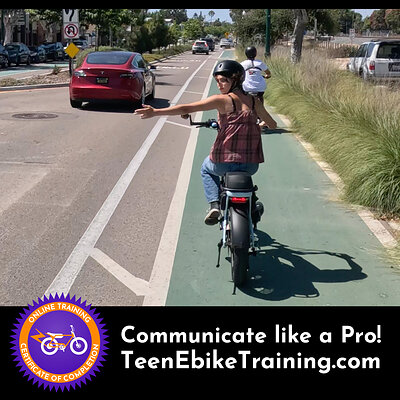 A teen on an ebike in a bike lane making a proper hand signal to turn left out of the lane.