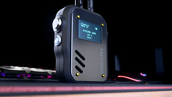 TACCOM v2 radio standing on a desk mat beside a backlit gaming keyboard and mouse
