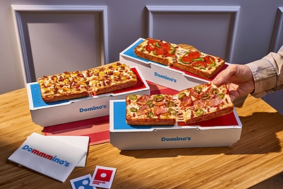 The Domino is made with premium, buttery-flavored pan dough encrusted with real Parmesan cheese and baked in a rectangular pan to create a crispy Parmesan Detroit-style crust. It is topped with two layers of cheese, customers' choice of sauce and up to three toppings, and finished with a drizzle of Domino's signature garlic seasoning.