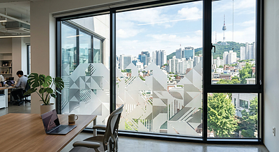 An office interior features geometric frosted graphics applied to large glass windows, providing visual privacy while preserving natural light and views of the surrounding cityscape.