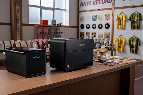 The HeyGears G1X Series desktop full-color 3D & UV printer and its post-processing unit are displayed on a table surrounded by various printed samples