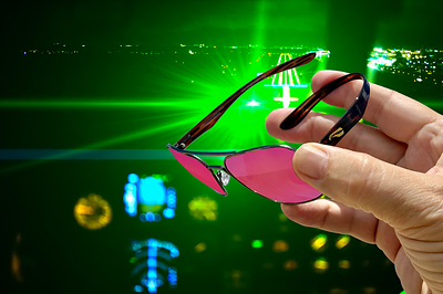 Photo illustration of a 532nm green laser strike on final approach at night, the scenario SentinelOps™ lenses are built for. Pilots reported 10,994 laser strikes to the FAA in 2025. Worn situationally during departure and arrival, the lenses reduce exposure below the eye injury threshold while leaving the rest of the visible spectrum, including instruments and approach lighting, clearly visible.