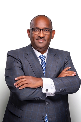Dexter Adderley, President and CEO of FOCOL Holdings Limited, stands with his arms crossed against a white background, wearing a dark blue suit, white shirt and blue striped tie.