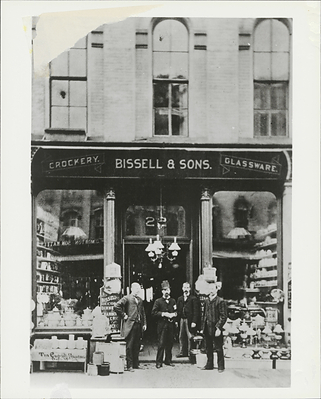 Black and white photograph print of the Bissell & Sons Crockery and Glassware Storefront, from the BISSELL Building History Scrapbook, 1876.