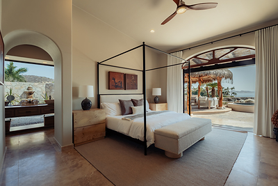 The primary suite pairs a canopy bed and travertine floors with arched doors that open directly onto a private terrace, palapa lounge and views of the Sea of Cortez.