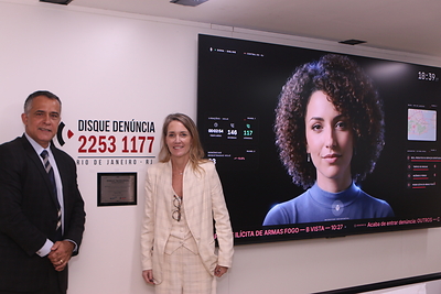 Diretor-geral do Disque Denúncia, Renato Almeida, com a CEO da BAT Brasil, Claudia Woods, ao lado da assistente virtual Dora, no painel da aplicação de Inteligência Artificial. | Crédito: Divulgação.