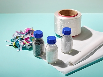 Products from each stage of the process, in which waste banners are finely shredded, chemically recycled into recycled materials, spun into yarn, and made into banners.