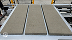 Three rectangular concrete slabs rest on a Samjung MetaBoard on a factory conveyor.