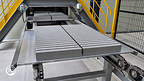 Rows of narrow concrete units rest on Samjung MetaBoards positioned on a chain conveyor beneath production equipment.