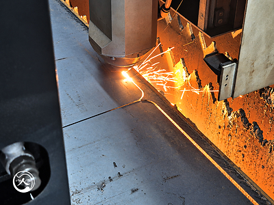 Close-up of a laser cutting head shaping a steel board profile, with sparks visible along the cut edge. Close-up of a laser cutting head shaping a steel board profile, with sparks visible along the cut edge.
