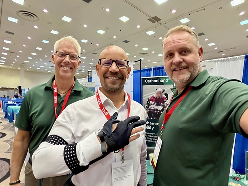 Mark Szymanski (center), CEO at Evocati PR, poses wearing the Carbonhand® alongside representatives from Bioservo at Paralyzed Veterans of America's Healthcare Summit + Expo 2026. (Source: Evocati PR)