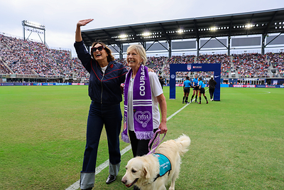 Actress and domestic violence advocate Mariska Hargitay walks onto the field with Cassidy, a Golden Retriever and Pet Partners therapy dog, and her handler Pat Eller during the pre-match at the U.S. Women's National Team match against Spain on October 10, 2026. Hargitay served as Purina's Honorary Captain to raise awareness for domestic violence survivors and their pets during Domestic Violence Awareness Month and in support of the Purple Leash Project. Credit to Purina