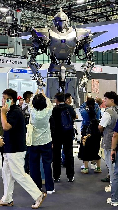 NeodraDynamics' silver and blue Neo1 humanoid robot towering over a crowd of visitors at its CIIF 2026 exhibition stand, several of them photographing it on their phones