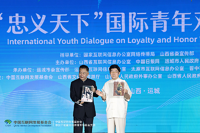 Li Zijun (right), a scholar of the Chinese Theatre Literature Society, displays a photo of his grandfather, Li Hongchun, portraying the legendary Chinese figure Guan Gong during the International Youth Dialogue on Loyalty and Honor Without Borders in Yuncheng, Shanxi province, on Wednesday. [Photo by Zhu Xingxin/China Daily]