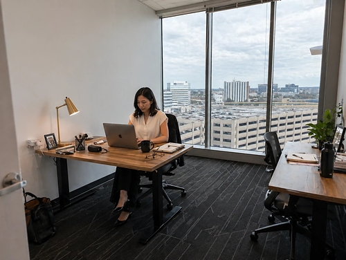 A member works at a desk beside floor to ceiling windows at e|spaces Orlando.