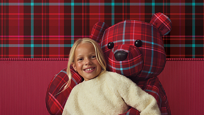 A young girl poses with a festive red-and-blue plaid bear. A young girl poses with a festive red-and-blue plaid bear.